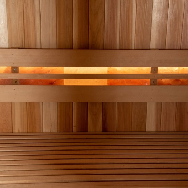 A close-up of the Almost Heaven Denali 6 Person Indoor Sauna interior, showing a smooth wood bench and backrest, plus a warm illuminated panel set into vertical cedar sauna planks by Almost Heaven.