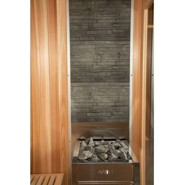The Almost Heaven Denali 6 Person Indoor Sauna by Almost Heaven features a metal sauna heater with dark stones, set against gray stacked stone tiles and surrounded by light wood paneling for a luxurious look.