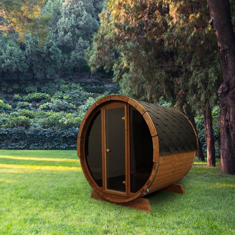The SaunaLife Model E7G 4 Person Barrel Sauna w/ Glass Front, a compact wooden barrel sauna by SaunaLife, sits on a grassy lawn surrounded by tall trees—a stylish and inviting outdoor retreat for ultimate relaxation.