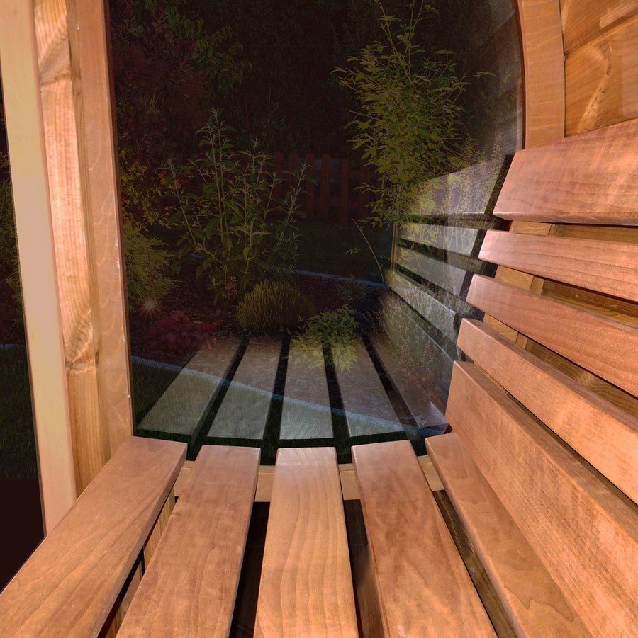 A wooden bench inside a shelter at night, with slats casting shadows, evokes the comfort of the SaunaLife Model E7G 4 Person Barrel Sauna w/ Glass Front, where a garden is visible outside through its transparent window.