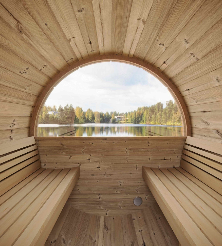 The SaunaLife Model E6W 3 Person Sauna Barrel-Window features Thermo-Spruce wood and curved benches, offering serene views of a calm lake and trees through its large arched window.