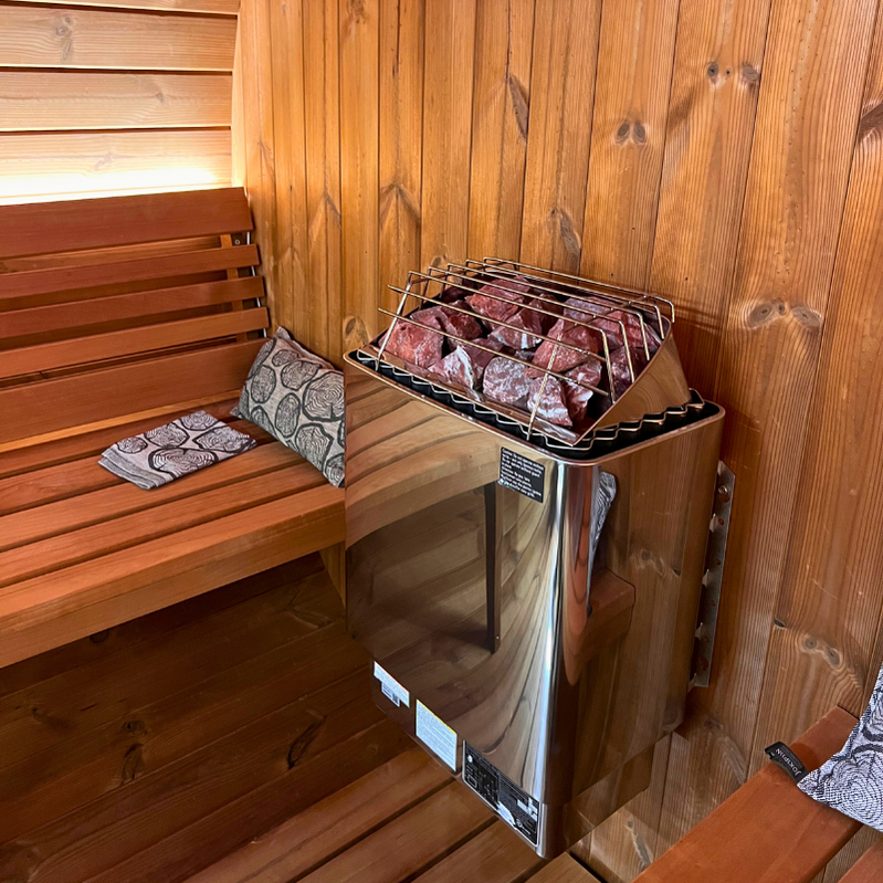 The SaunaLife Model E8 6 Person Barrel Sauna by SaunaLife features a wooden interior, metal stone-filled heater, wall-length bench, and patterned cushions for comfort.