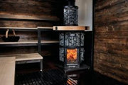 The Harvia Legend 240 GreenFlame Sauna Stove by Harvia is a modern wood-burning sauna stove with a glass door showing the fire, set against dark wooden walls and benches; a basket rests on a shelf in the background, offering an authentic sauna experience.