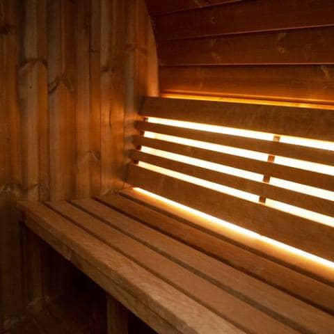 The SaunaLife Model E6W 3 Person Sauna Barrel-Window features a Thermo-Spruce bench and warm ambient lighting through the slats, creating a cozy, inviting atmosphere for your ultimate relaxing retreat.