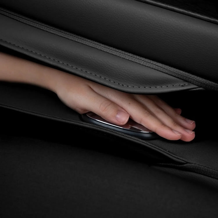 A hand reaches between two black leather car seats of the Osaki 4D Orion Duo Mech Massage Chair to retrieve a smartphone from the seat gap, showcasing smart features beyond its advanced AI massage experience.