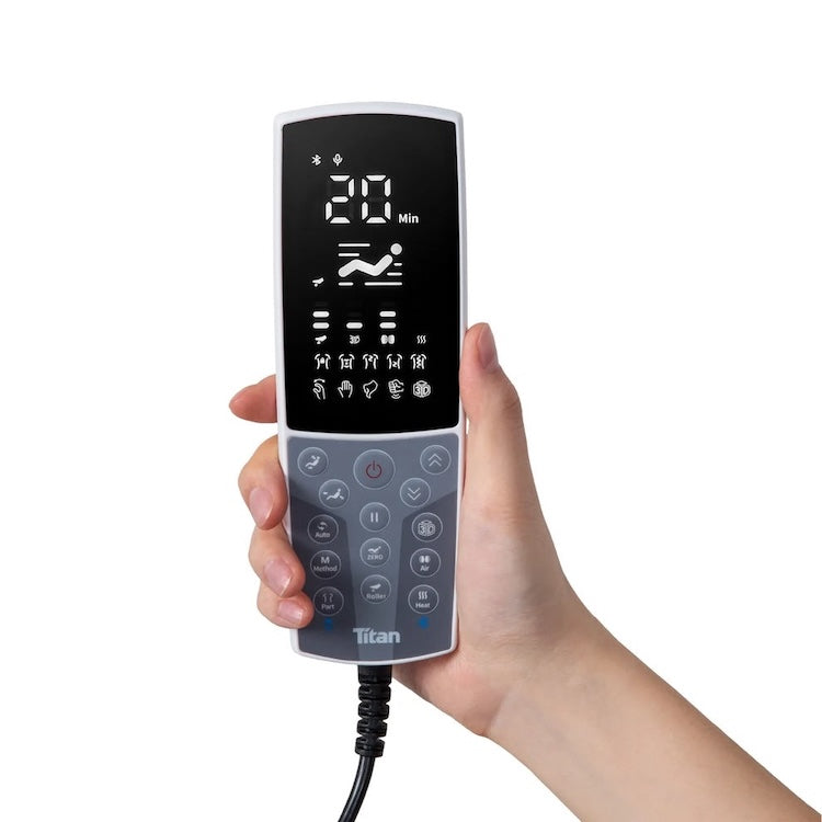 A hand holds a Titan remote with a digital display showing time, massage settings, and buttons—perfect for adjusting the Titan Grande XL 3D Massage Chair or activating zero-gravity recline during a full body massage.