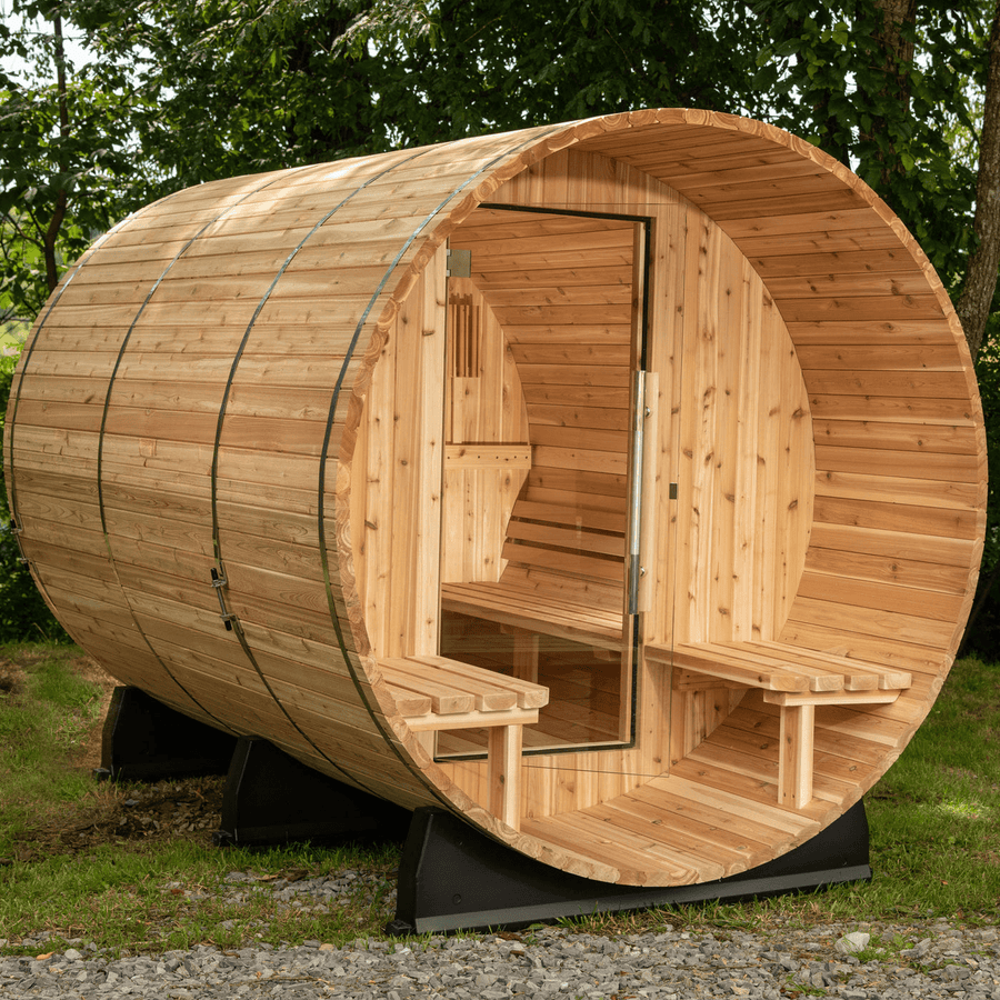 The Almost Heaven Charleston 4 Person Canopy Barrel Sauna by Almost Heaven features a cylindrical wooden design, glass door, benches, and a Harvia 6kW heater, set outdoors on grass and surrounded by trees.