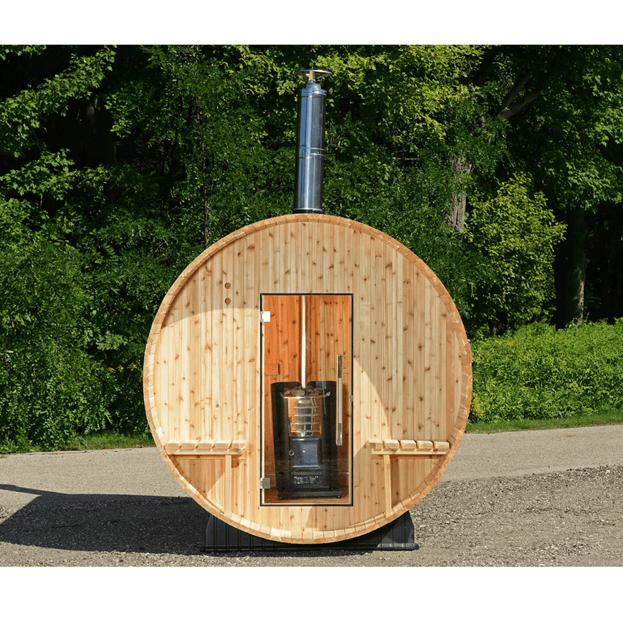 The Almost Heaven Grandview 4-6 Person Canopy Barrel Sauna features a front door and metal chimney, nestled on gravel among green trees—perfect for relaxing outdoor moments in nature.