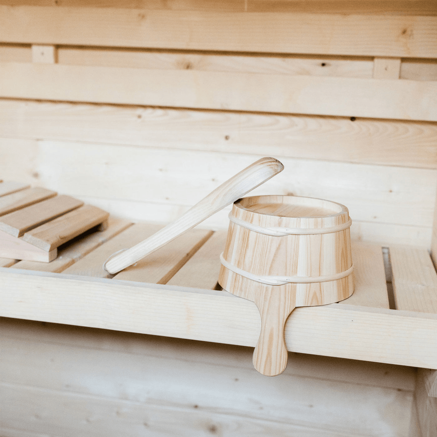 A wooden bucket with a ladle sits on a bench inside the Almost Heaven Timberline 6 Person Cabin Sauna, showcasing the natural wood textures and minimalist design of this inviting Almost Heaven sauna.