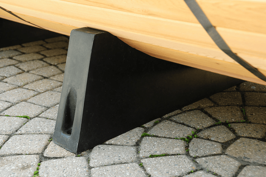A close-up of a sturdy black support stand holding up a wooden section of the Almost Heaven Vienna 2 Person Canopy Barrel Sauna, placed on circular stone paving with small patches of green moss.