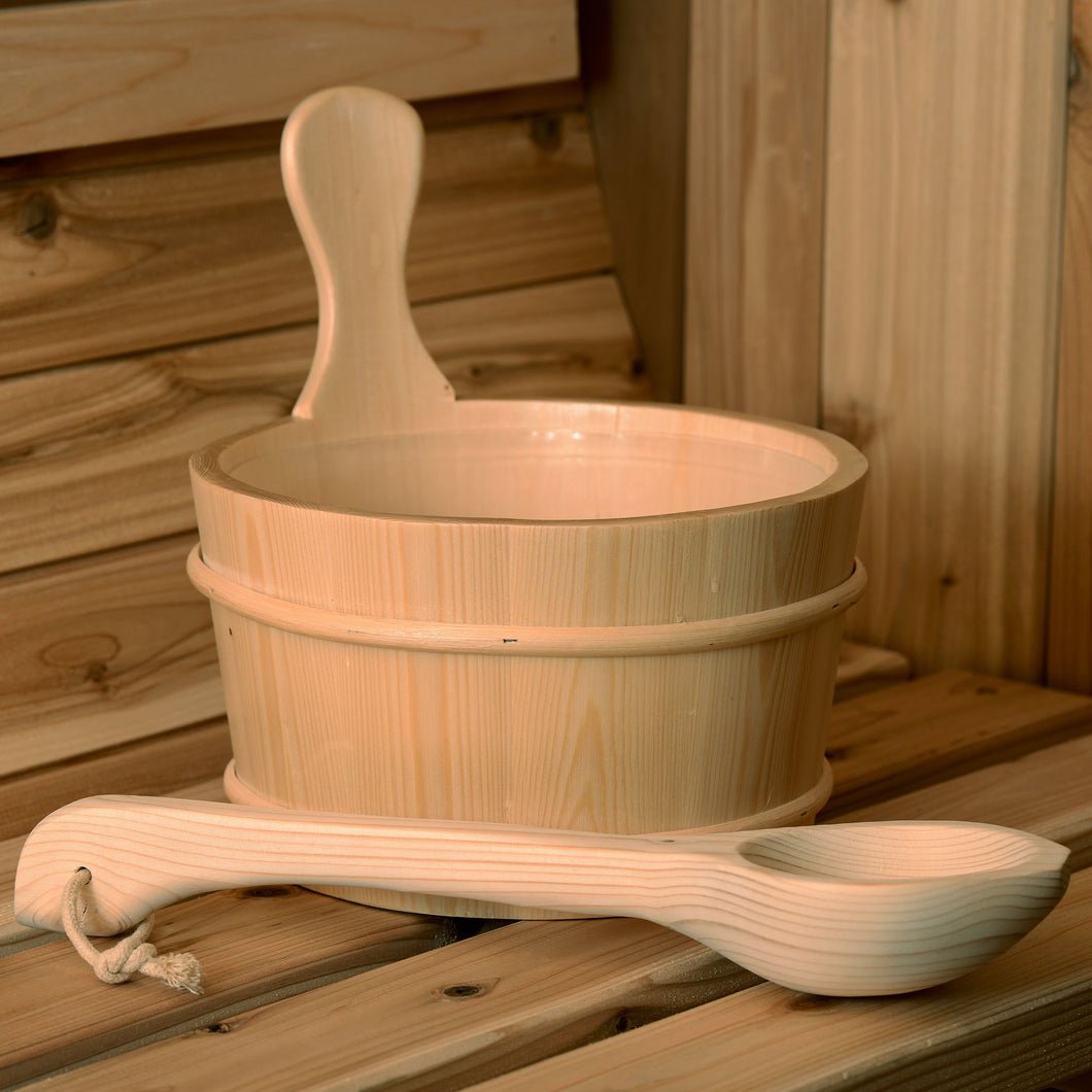 The Almost Heaven Bucket, Ladle, and Thermometer Package by Almost Heaven rests on a bench amid wood paneling—classic sauna accessories that enhance the peaceful atmosphere.