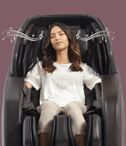 A woman relaxes in the Daiwa Hubble Massage Chair by Daiwa, eyes closed in comfort as airbag massage soothes her. Musical notes above her imply she's enjoying music while sitting back in this wall-hugger chair, dressed in a white blouse and beige pants.