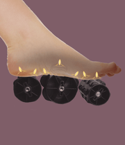A bare foot presses on three black foam rollers with yellow lights highlighting pressure points, illustrating Daiwa Hubble Massage Chair's airbag massage technology, set against a plain mauve background.