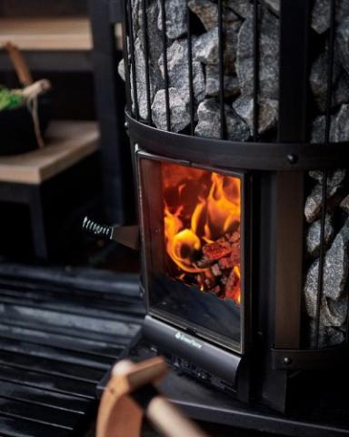 A close-up of the Harvia Legend 240 GreenFlame Sauna Stove by Harvia, showing flames through the glass door and stones enclosed in a sleek black metal frame.