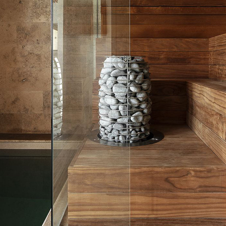 Modern wooden sauna interior with smooth benches and walls, a glass wall, and the HUUM HIVE Mini Series 10.5kW Sauna Heater Package by HUUM as the centerpiece, plus a visible stone pool just outside the sauna area.