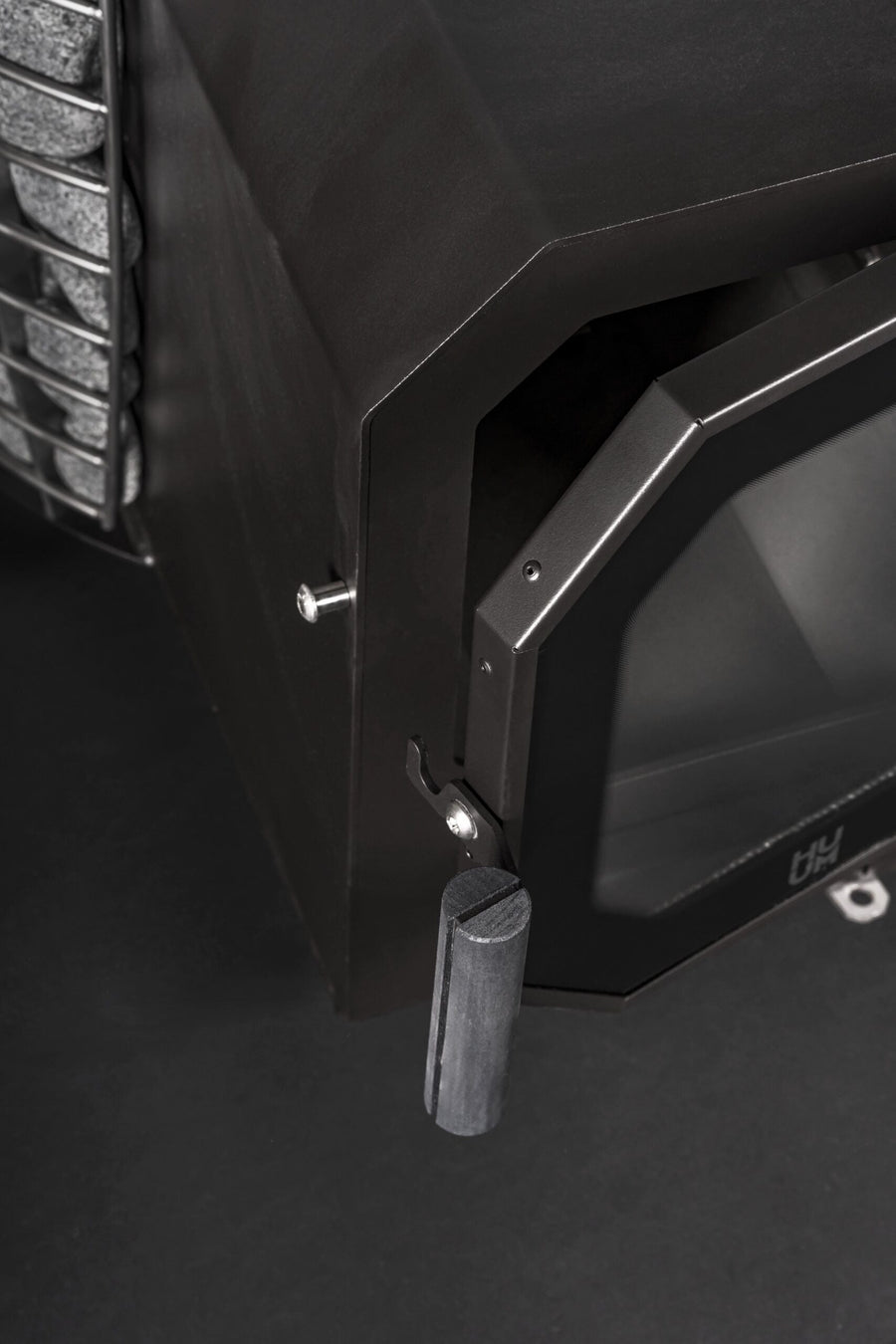 Close-up of the HUUM Hive Flow LS Wood Burning Sauna Stove by HUUM, featuring a black metal body, open angular glass door with a cylindrical handle, and visible stone compartment—ideal for any HUUM Hive Flow sauna heater setup.