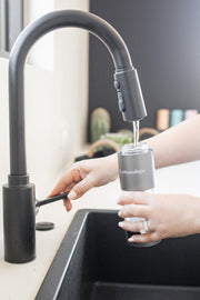 A person fills the Mito Red Light MitoHYDRO™ Ultra Premium Hydrogen Water Bottle at a kitchen sink, holding it under the faucet to enjoy antioxidant-rich hydrogen water.
