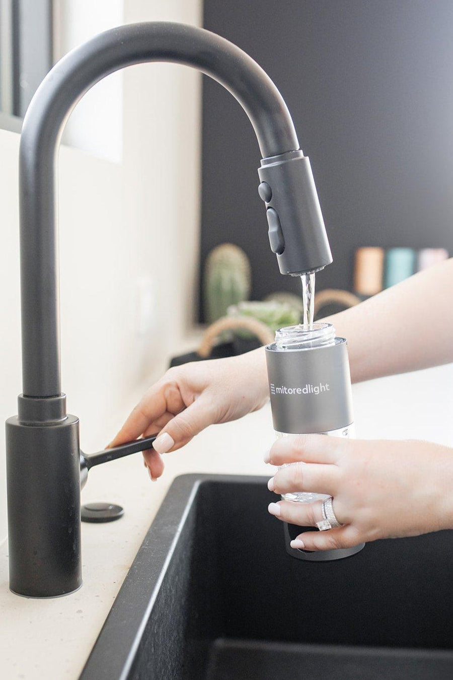 A person fills the Mito Red Light MitoHYDRO™ Ultra Premium Hydrogen Water Bottle at a kitchen sink, holding it under the faucet to enjoy antioxidant-rich hydrogen water.