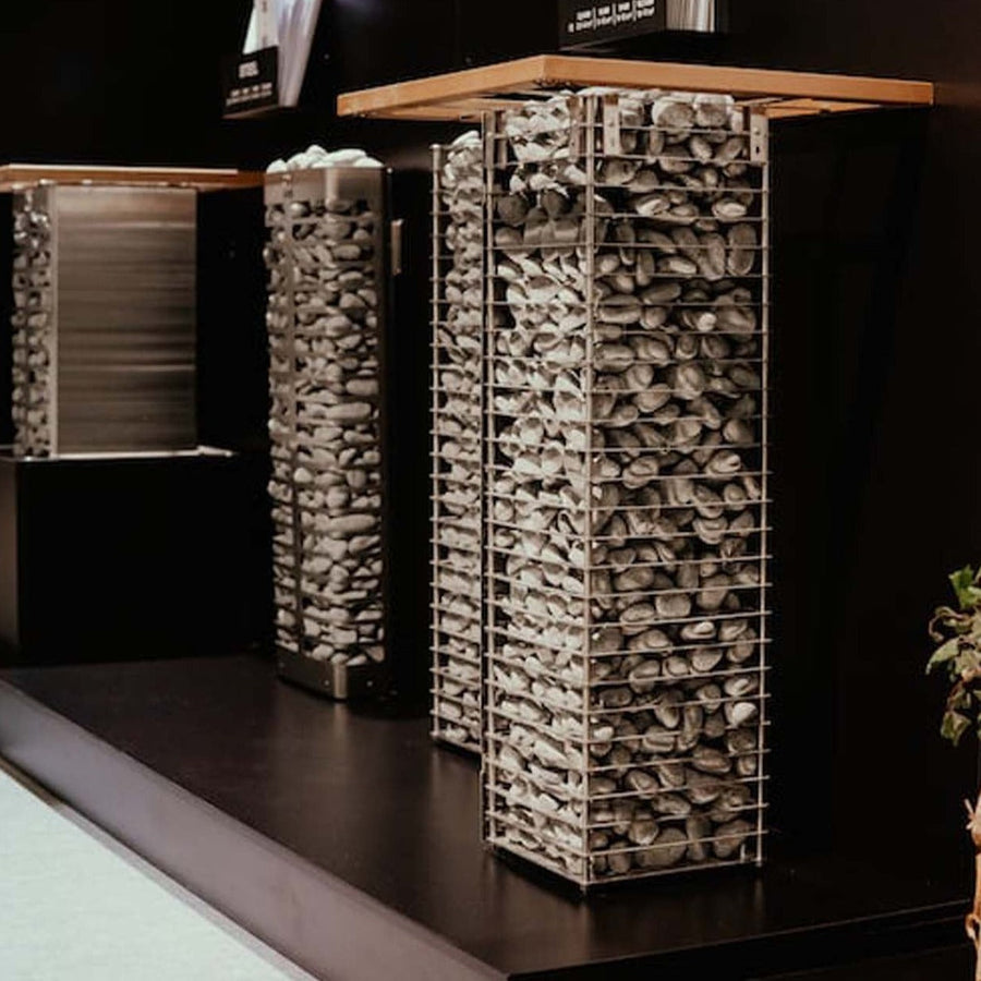 Tall, rectangular metal cages filled with smooth gray stones and wooden tops are set against a dark wall, echoing the contemporary, minimalist look of the HUUM CLIFF Series 11kW Sauna Heater Package by HUUM.