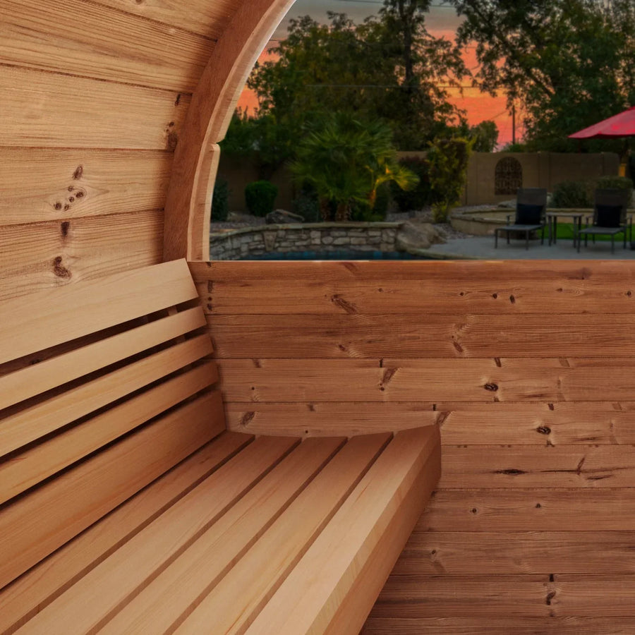 Interior view of the SaunaLife Model E8W 6 Person Sauna Barrel-Window by SaunaLife, featuring a curved wall and bench, with views of a backyard pool, trees, and sunset sky in the background.