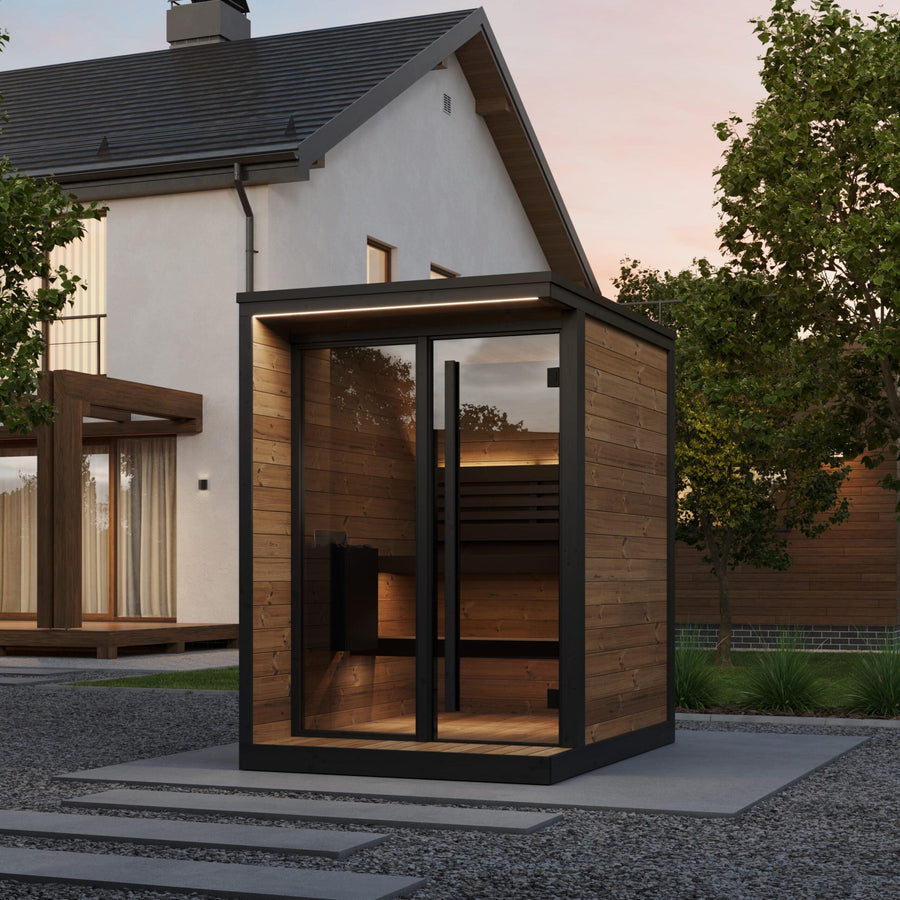 The SaunaLife Model GL4 4 Person Garden Luxury Series Outdoor Sauna Kit by SaunaLife sits in a landscaped backyard near a modern home, featuring glass doors and windows, surrounded by trees at dusk.