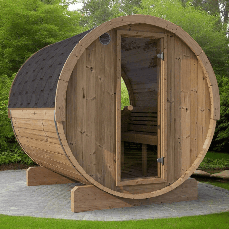 The SaunaLife Model E8W 6 Person Sauna Barrel-Window by SaunaLife features a barrel shape and glass door, set on a stone patio among lush greenery and trees in a garden.