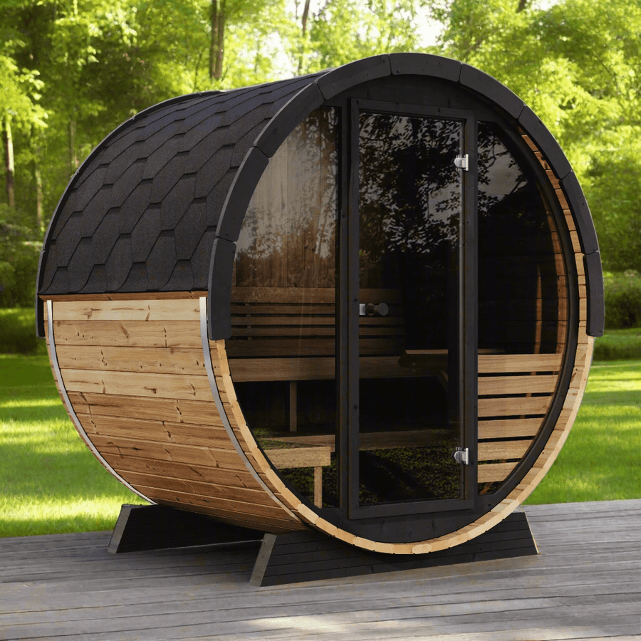 The SaunaLife Model EE6G 4 Person Barrel Sauna by SaunaLife, featuring a black shingled roof and glass door, sits on a wooden deck with green grass and trees in the background.