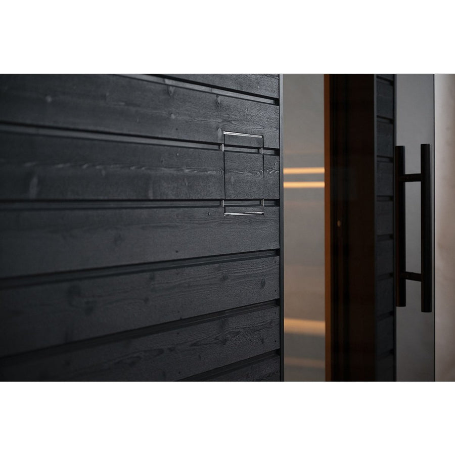 A close-up of the SaunaLife G6 5-Person Outdoor Cabin Sauna shows its modern black wooden wall with horizontal panels and a sleek metal handle by a glass door with a large black handle, softly lit from inside this stylish outdoor sauna by SaunaLife.