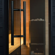 Close-up of a sleek black metal handle on the glass door of the SaunaLife G6 5-Person Outdoor Cabin Sauna, with warm lighting and sauna stones softly blurred in the background.