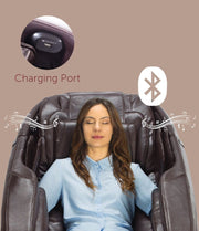 A woman relaxes in the Daiwa Majesty Massage Chair by Daiwa, eyes closed as musical notes and a Bluetooth icon indicate wireless audio. An inset shows a charging port, while a soft brown background enhances the full-body massage experience.