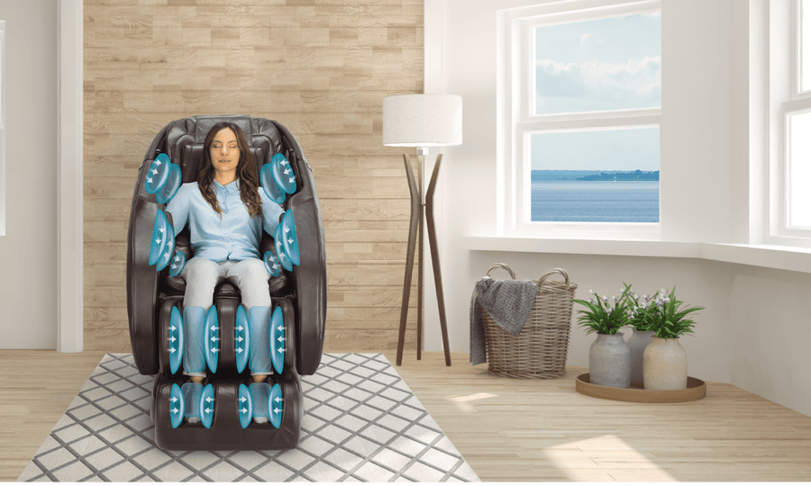 A woman relaxes in a Daiwa Majesty Massage Chair by Daiwa as blue graphics highlight its 3D body scan technology targeting arms, legs, and back. Sunlight streams through large windows with indoor plants for a calming ambiance.