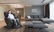 A man in business attire relaxes in a Daiwa Relax 2 Zero 3D Massage Chair by Daiwa, enjoying stress relief in a modern living room with neutral-toned decor.