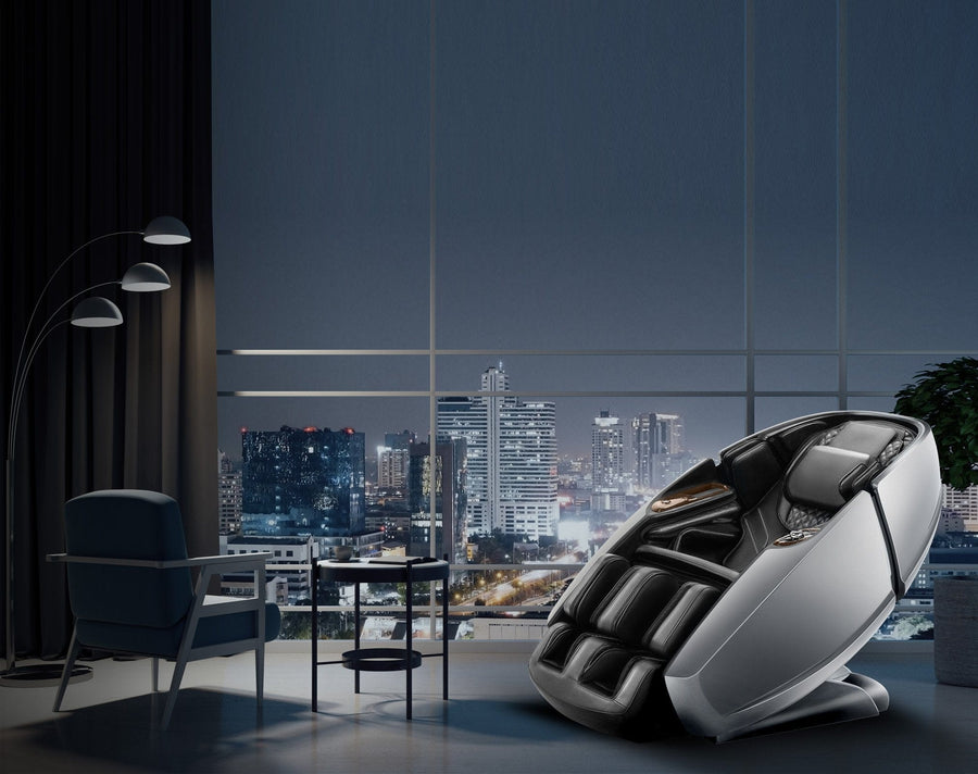 A Daiwa Supreme Hybrid Massage Chair by Daiwa sits near large windows with a city skyline view at night, beside a small table, armchair, tall floor lamp, and potted plant in a stylish, dimly lit room.