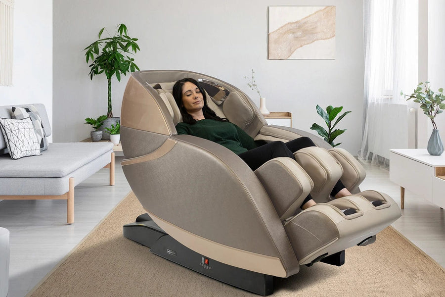 A woman relaxes in a Kyota Kansha M878 Massage Chair by Kyota in a bright, modern living room with minimalist décor, featuring a potted plant, wall art, and light furniture.