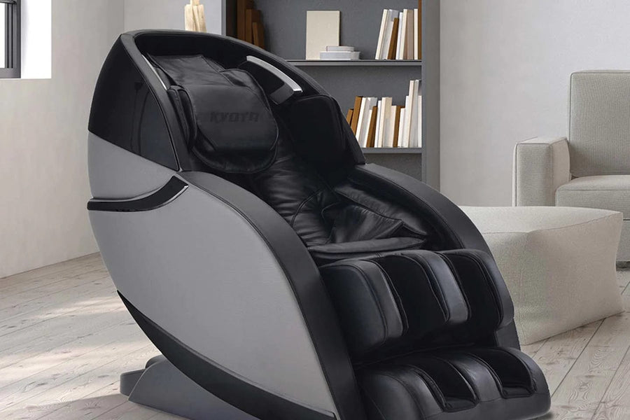 The Kyota Kansha M878 Massage Chair by Kyota, in black and gray, features padded leg, arm, and head supports plus a sleek 4D design—shown in a bright room with wooden floors and a bookshelf behind it.