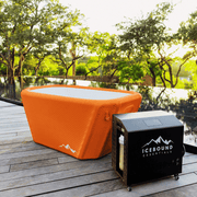 The Big Tex Endurance Plunge Tub by Icebound Essentials, in burnt orange, sits on a wooden deck beside a black Icebound Essentials cooling unit, surrounded by green Texas trees and sunlight.