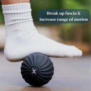 Someone wearing a white sock rolls their foot over the black Icebound Essentials VibePro Pulse massage ball on a wooden floor. Text: "Break up fascia & increase range of motion.