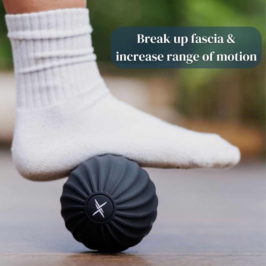 Someone wearing a white sock rolls their foot over the black Icebound Essentials VibePro Pulse massage ball on a wooden floor. Text: "Break up fascia & increase range of motion.