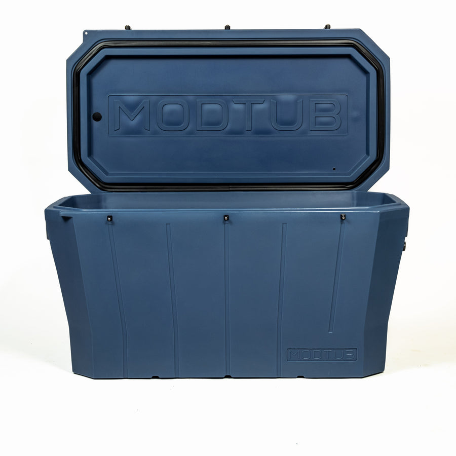 A large, blue Modtub 2.0 Cold Plunge tub by Modtub is shown with its lid open, revealing a spacious interior. The rectangular plastic build is sturdy and features a subtle geometric design on the front.