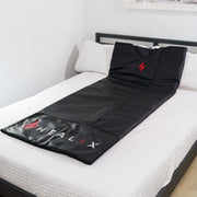 The HEALiX Infrared Sauna Blanket with built-in pillow is displayed on a white bed, bringing a spa-like relaxation experience to your bright, minimalistic bedroom.