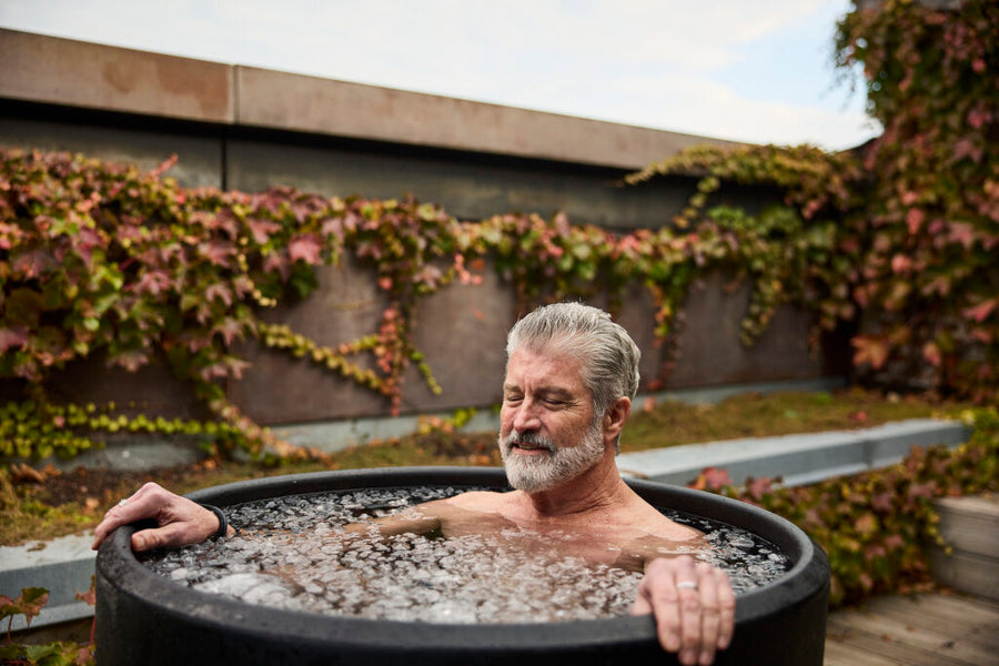A man in the Ice Barrel 300, an insulated cold therapy tool, seated upright in a tub of ice.