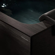 Close-up of the Kohler x Remedy Place Ice Bath, a dark wood tub filled with water for cold immersion, featuring the Kohler brand name engraved on the side and a black headrest on its edge.