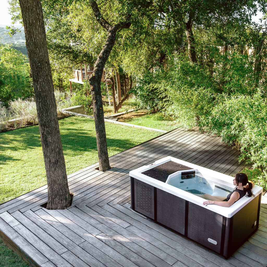 Relax alone with professional-grade recovery in The Resolute Pro by Icebound Essentials, surrounded by trees on a wooden deck as sunlight streams through the leaves for a peaceful outdoor soak.