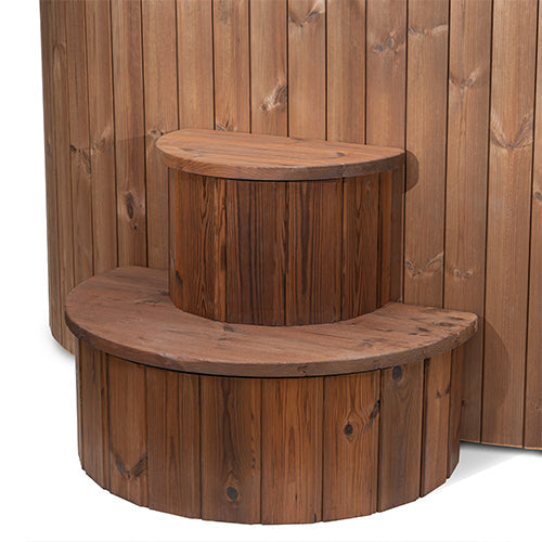 Two semi-circular, vertically paneled wooden steps from SaunaLife provide easy access to the SaunaLife Model S2NC – a 2-person immersion tub with a natural finish chiller and heater, perfect for home spa or sauna setups.
