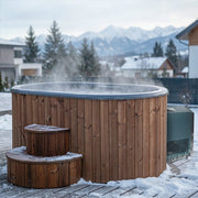 The SaunaLife Model S2NC – 2-Person Immersion Tub with Natural Finish Chiller & Heater by SaunaLife sits steaming on a snowy deck, steps dusted in snow, surrounded by evergreens and mountains for a cozy home spa retreat.