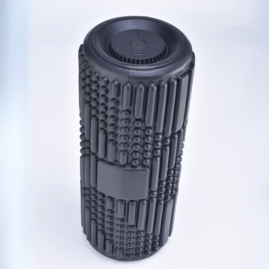 The VibePro Flow by Icebound Essentials is a textured black cylindrical vibration roller with a patterned surface. Viewed from above on a white background, it has a control button and indicator lights for customizable deep massages.