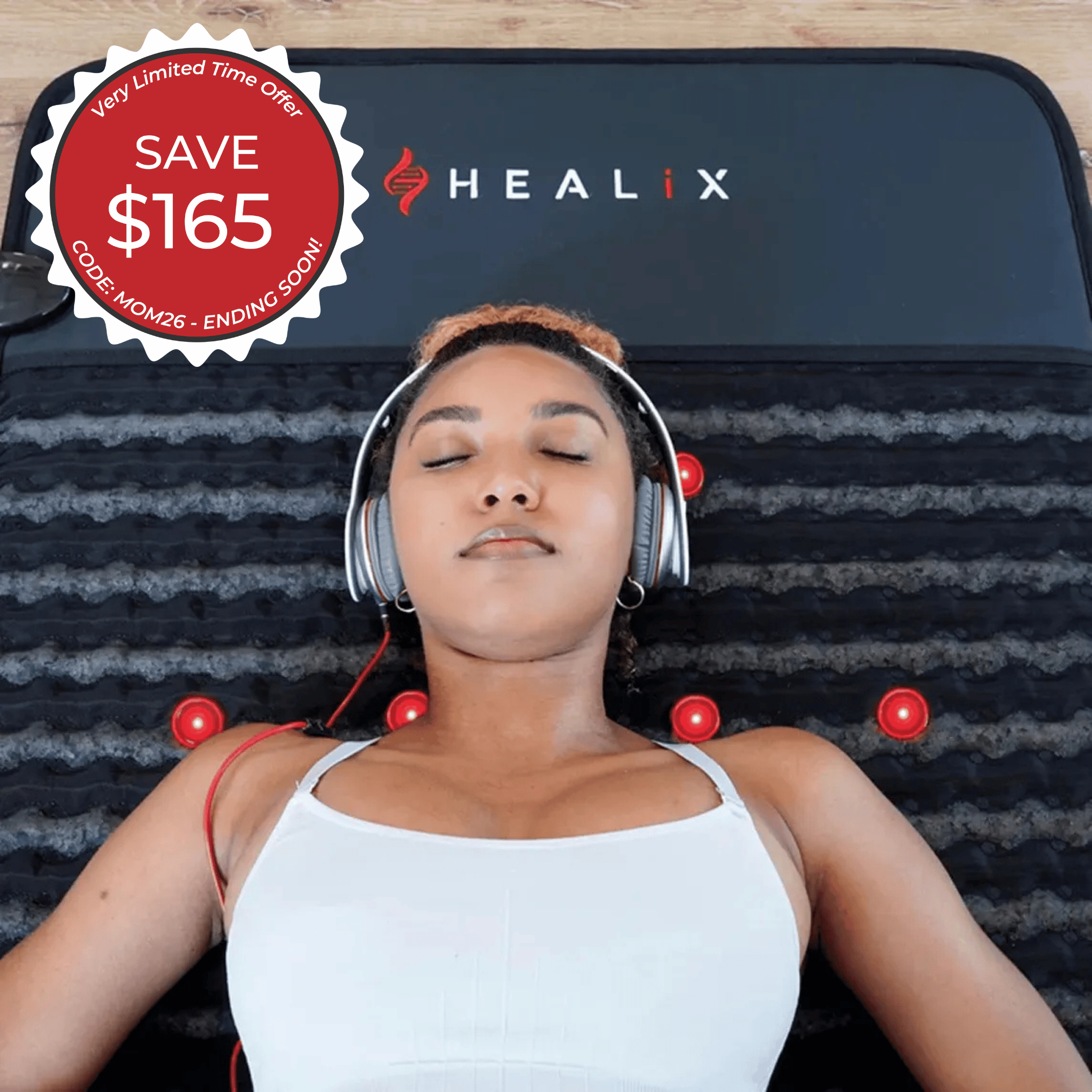 A woman in headphones relaxes on a black HEALiX Infrared Revive PEMF Mat with raised nodes. A red badge reads: SAVE $165, Very Limited Time Offer, CODE AMON26 - ENDING SOON.