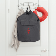A gray backpack with a red DNA logo, gray towel, and red neck pillow hang on hooks—perfect accessories to pair with your HEALiX Infrared Stash or sauna blanket carrying bag.