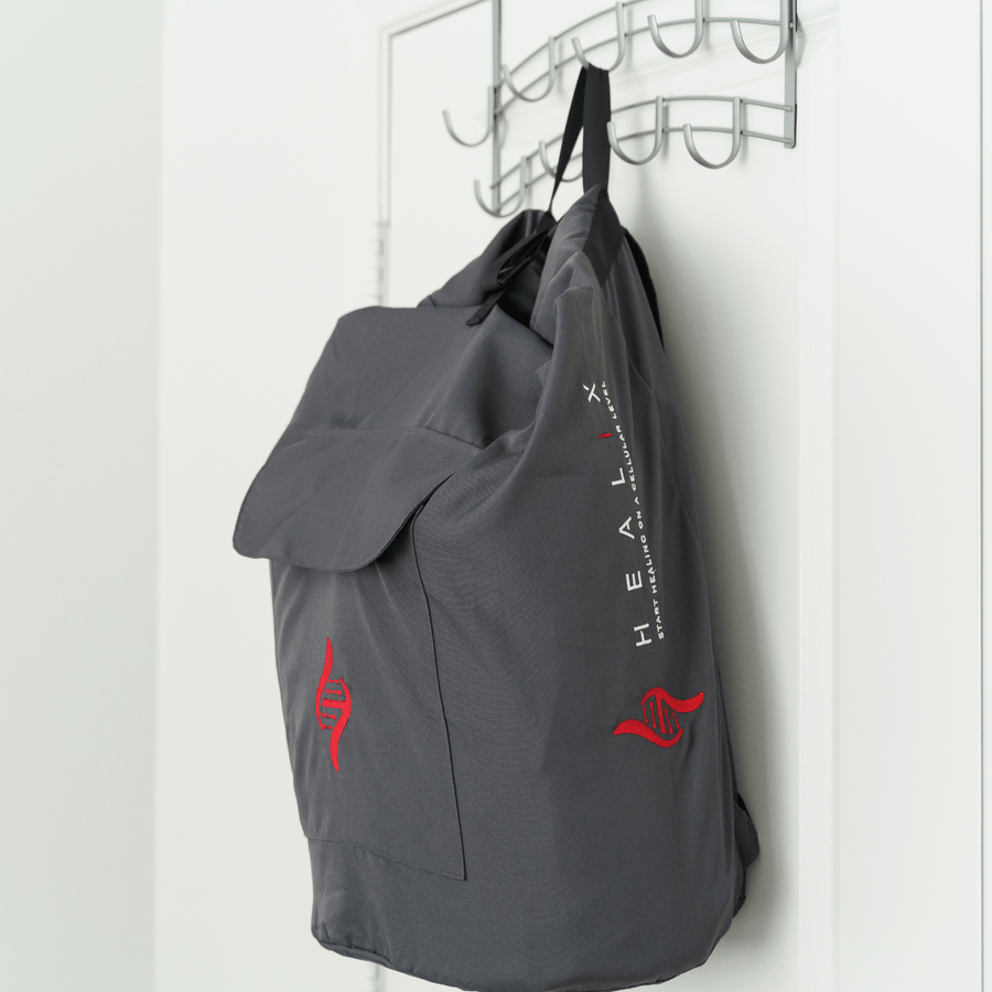 A gray HEALiX Stash backpack by HEALiX Infrared, featuring red DNA helix designs and branding on the side, hangs from a hook rack on a white door—ideal for carrying therapy device accessories.