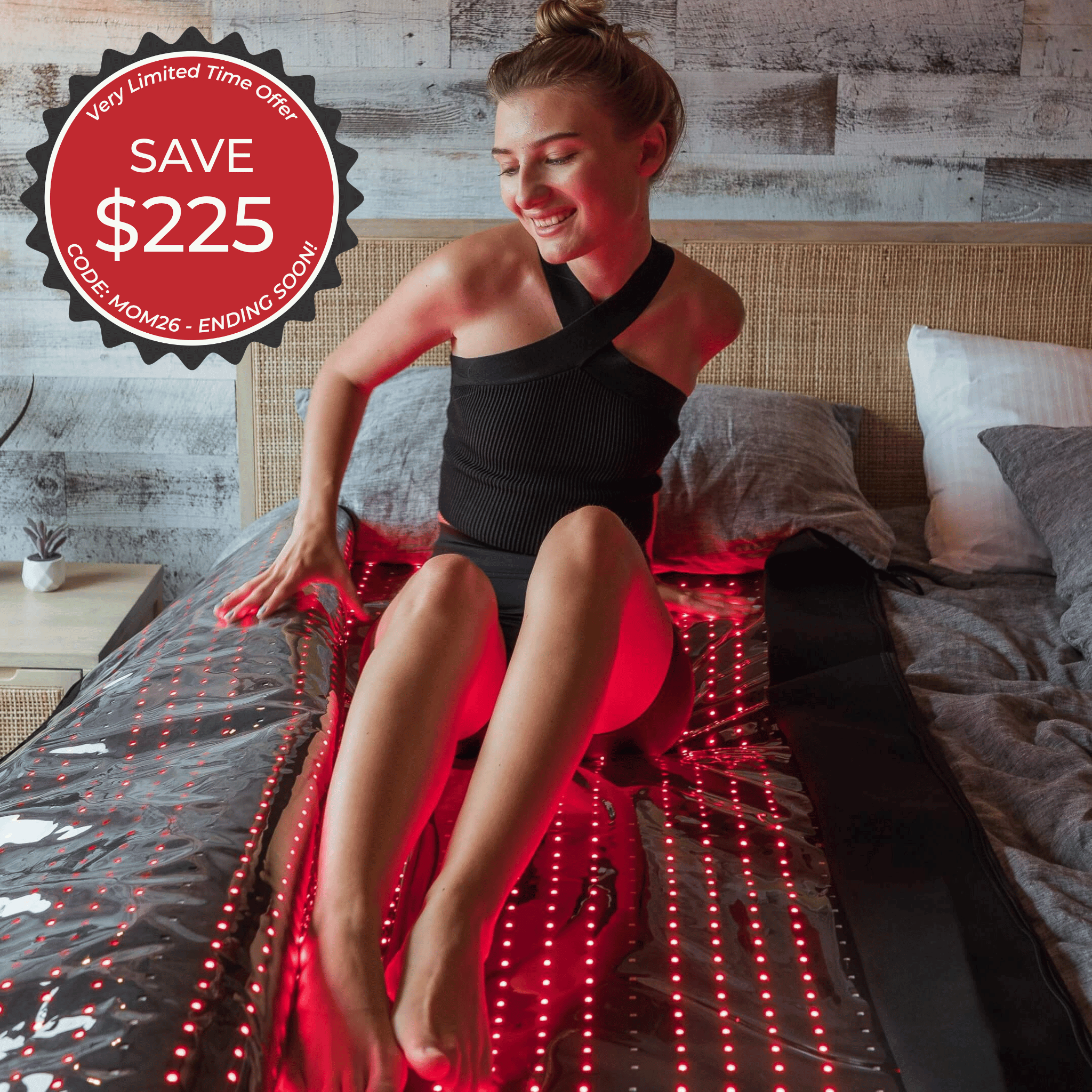 A woman in black sits on a HEALiX Glow Pod red light therapy mat by HEALiX Infrared, smiling. Save $225 with code MOM26—ending soon. Very limited time offer! Advanced wellness via near infrared technology.